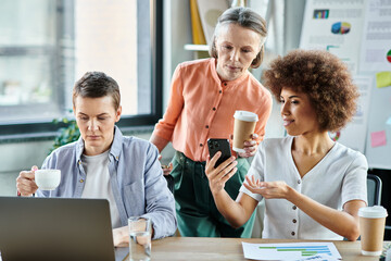 Diverse female professionals gathered around a laptop on a table in a collaborative workspace.
