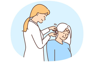 Female doctor install hearing aid to old patient