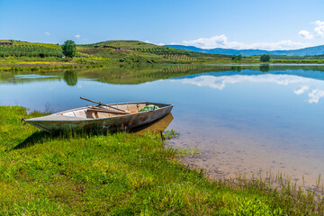 Naklejka premium A view past a boat out across a lake at Belsh lakes in Albasan county, Albania in summertime