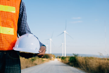 Engineer with safety helmet stands at wind turbine field. Represents renewable success innovation...