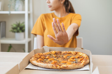 Diet concept, unhappy asian young woman, girl refusing to eat Pizza in box at home, hand pushing...