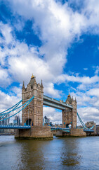 Obraz premium Diagonal view of London's Tower Bridge with its reflection in the River Thames under a blue sky with white clouds. United Kingdom.