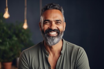 Obraz premium Portrait of a smiling indian man in his 40s smiling at the camera while standing against modern minimalist interior