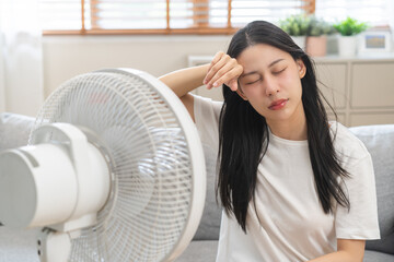 Suffer summer heat wave stroke, hot weather, tired asian young woman sitting on couch in living...