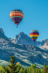 A breathtaking sight of vibrant hot air balloons drifting gracefully over a majestic mountain range, against a backdrop of clear blue skies, symbolizing adventure, and exploration