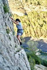 A boy is scaling a steep cliff using a rope to support her ascent. She is focused and determined as...