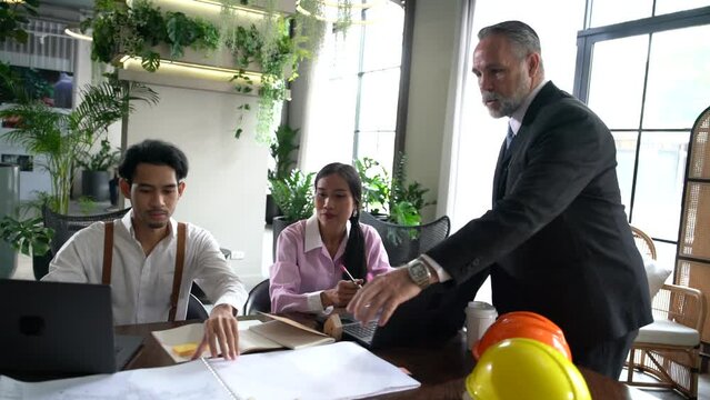 senior male manager in a suit discusses planning, consulting, construction, real estate development with ทีมงานพนักงานและ female secretary at a table and a laptop in a company meeting room