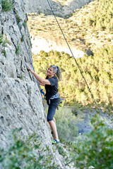 A woman is climbing up a cliff in the mountains, showing determination and strength