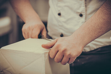 Obraz premium Baker cuts butter from a big block