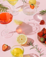 Summer refreshment, alcoholic drinks, fruit cocktails with strawberries, lemon slices and rosemary branches in the shade of tropical leaves.