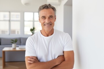 Portrait of a blissful man in his 50s with arms crossed while standing against modern minimalist interior
