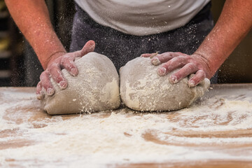 A baker kneads bread dough in the bakery. Vintage style with grain. Vertical.