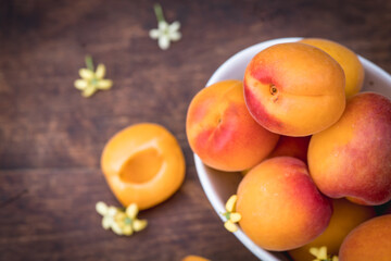 White ceramic bowl with ripe apricots on a wooden table in the garden