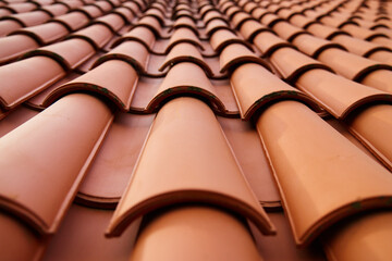 Red ceramic roof tiles covering residential building roof. Tile pattern close-up