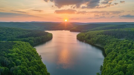 A serene aerial view of a sunset over a calm lake surrounded by lush woodlands. - Powered by Adobe