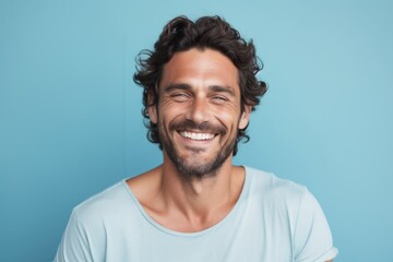 Fototapeta premium Portrait of a blissful man in his 30s smiling at the camera in front of pastel blue background
