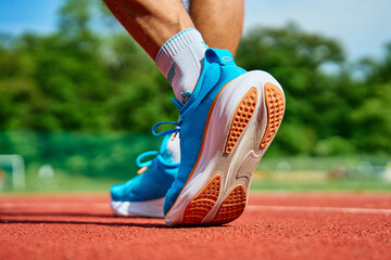 Athlete wearing bright blue running shoes on red stadium track during training. Sportsman legs in...