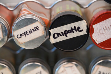Cayenne and chipotle spice masking tape label on spice jar in spice rack.