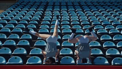 Two fiery women joyfully dancing on a stadium track. Slow motion shooting. Women cheerleaders in short skirts happily dancing on the running track. Two girls in bras seductively dancing together on a 