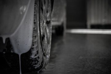 Close-up of a car wheel along which foam flows onto the floor of the car wash. The car is covered...