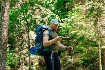 Adult man standing and browsing smartphone in green forest in daylight