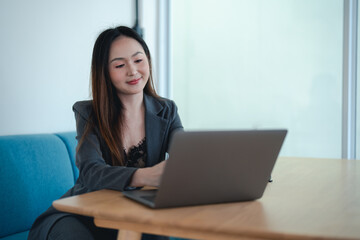 Fototapeta premium Asian young beautiful happy professional successful businesswoman designer sitting smiling at workstation desk using laptop notebook computer and smartphone working remotely online at home office