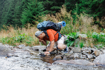 Male hiker drinking water from creek in forest