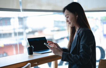Fototapeta premium Asian young beautiful happy professional successful businesswoman designer sitting smiling at workstation desk using laptop notebook computer and smartphone working remotely online at home office