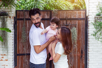 Joyful family moment with both parents playing with their toddler daughter in a garden, expressing...