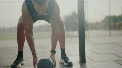 Determined male athlete in intense outdoor fitness session stretches with a medicine ball, showcasing strength and flexibility. Focused Young Man in Outdoor Workout Stretching with Medicine Ball