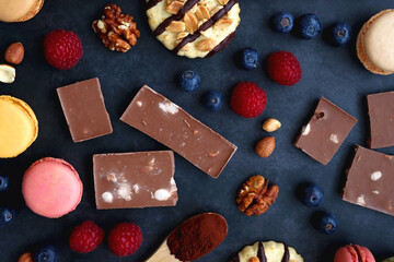 Macarons, chocolate, cookies, berries and various nuts on dark blue background. Top view.