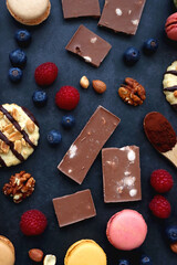 Macarons, chocolate, cookies, berries and various nuts on dark blue background. Top view.