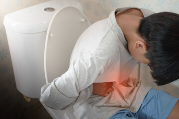 Asian boy sitting on toilet and holding his stomach with stomach pain causes of constipation or...