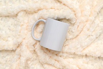 White mug on white fur texture. Dishes for tea and coffee. View from above.