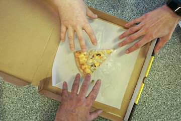 Three hands of three men reach for one piece of pizza that remains in the box.