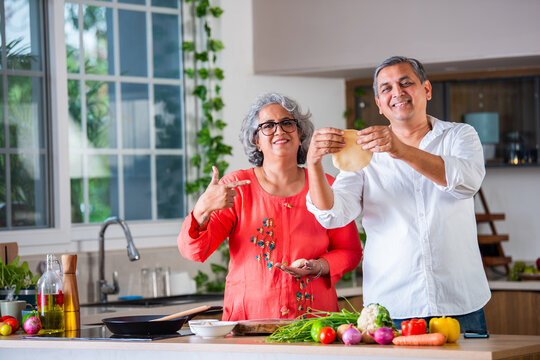 Indian asian senior woman teaches husband how to cook, to make a round chapati or roti