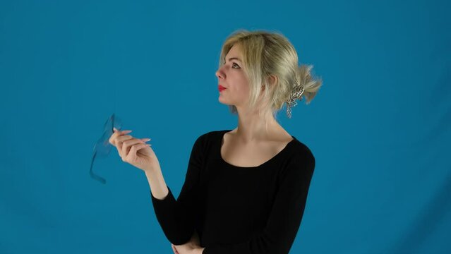 Woman worker twists glasses thinking or dreaming and sighs in dissatisfaction on blue background. Businesswoman repetitive motions reflect turmoil