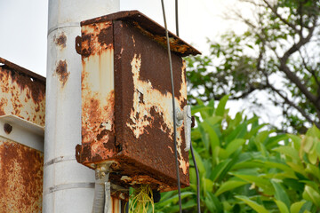 Broken and rusted electrical control box or electric Switchboard on electrical pole at outdoor park with forest and sky background.