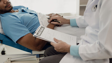 A young man lies on a bed in a hospital ward talking with her young Indian doctor. Doctor checking patient's health doctor treating patient, hospital admission of patient