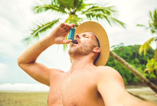 Man with inhaler having asthma attack outdoors on beach