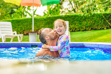 father with little girl in pool on sunny day.