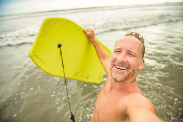 Summer beach fun surfer man running with bodyboard on selfie style