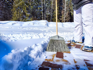 Clearing Snow From Sunny Yard With Broom. Person sweeps fresh snow off the brick path in front of a...