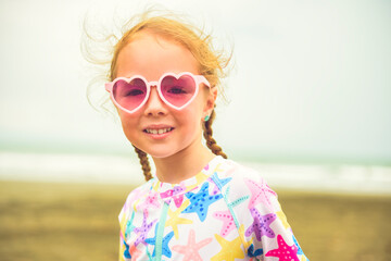 Portrait of laughing girl of 4 years with heart-shaped sunglasses on beach of Costa Rica