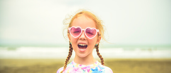 Portrait of laughing girl of 4 years with heart-shaped sunglasses on beach of Costa Rica