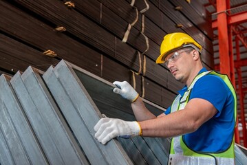 A worker wearing a hard hat and safety vest inspects metal beams at a warehouse.