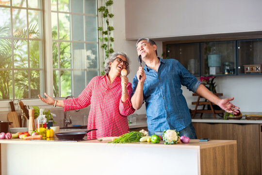 Indian asian retired old senior couple singing in kitchen while cooking food