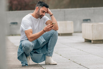 attractive young adult man with beard outdoors looking worried at mobile phone