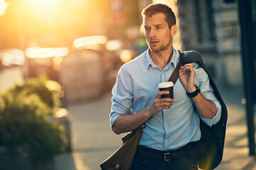 Businessman walking in city with coffee during sunset