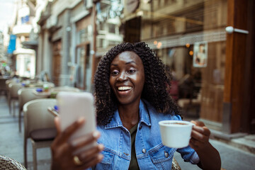 African American woman enjoying coffee and taking selfie at street cafe